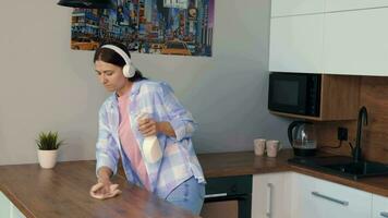alegre mujer limpia el Departamento y bailes mientras escuchando a música en auriculares. video