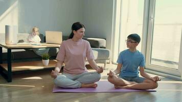 mamá y hijo meditar a hogar sentado en el piso cerca el ventana. video