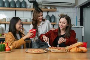 A group of young female friends have a party with pizza on the table and red drink glasses. Talk and live together happy, having fun at home. photo