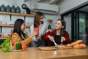 A group of young female friends have a party with pizza on the table and red drink glasses. Talk and live together happy, having fun at home. photo