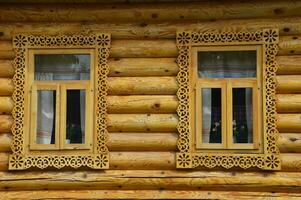 Two windows with carved frames of a brown wooden house. Wooden log village house. photo