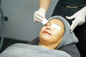 Cosmetologist use a cotton pad to prepare receiving skin gel and color light therapy to stimulate facial health on woman client face in beauty clinic. photo