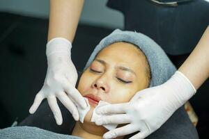 Cosmetologist use a cotton pad to clean on woman client face in beauty clinic. photo