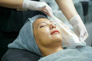 de cerca cosmetólogos limpieza el cara de asiático belleza mujer antes de haciendo cara spa y facial mascarilla. foto
