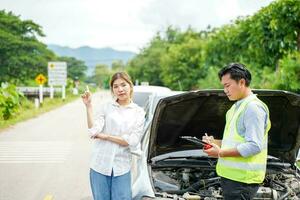 Closeup insurance company officers post a list of repairs on work list clipboard with woman driver acting point beside car accidents on road side. photo