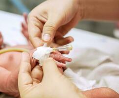 Nurse hands using medical adhesive plaster stick and wrap safely on IV Catheter and sick newborn baby's hand  for prepare fill the saline solution and medicine. photo