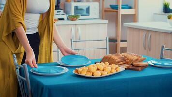 Close up of a middle aged woman and older senior have fun working together setting the dinner table in kitchen, while men talking in background during a relaxing family day. photo