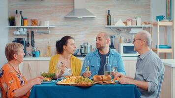 extendido familia hablando teniendo relajante tiempo. multi Generacion disfrutando hora a hogar, en el cocina sentado por el mesa, comiendo cena juntos y Bebiendo foto