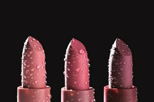 Three moisturizing lipsticks with water drops on a dark background. photo