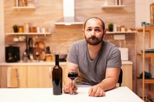 Thoughtfull young man holding a glass of red wine thinking about life problems. Unhappy person disease and anxiety feeling exhausted with having alcoholism problems. photo