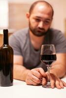 Man having alcohol addiction holding a glass of red wine. Unhappy person disease and anxiety feeling exhausted with having alcoholism problems. photo