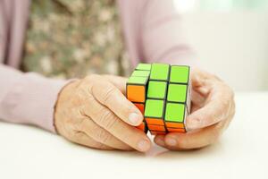 Bangkok, Thailand - May 15, 2022 Asian elderly woman playing Rubik cube game for treatment dementia prevention and Alzheimer disease. photo