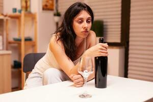 Lonely woman holding a bottle of red wine. Unhappy person suffering of migraine, depression, disease and anxiety feeling exhausted with dizziness symptoms having alcoholism problems. photo