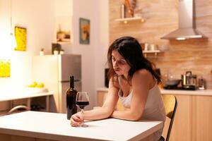 Woman with alcohol addiction and depression looking at glass with red wine. Unhappy person disease and anxiety feeling exhausted with having alcoholism problems. photo