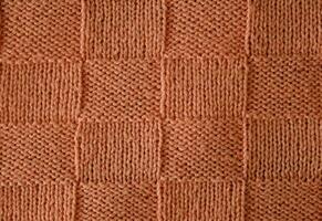 Texture of smooth knitted sweater with pattern. Handmade knitting wool or cotton fabric texture. Unusual abstract knitted chess pattern background texture. Peach Fuzz colour of 2024 year photo