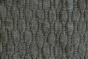 Texture of smooth knitted gray sweater with pattern. Top view, close-up. Handmade knitting wool or cotton fabric texture. Background with knitted leaf shape, knitting pattern with cables. photo