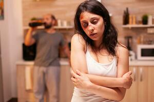 Scared woman after she gets a beating from drunk and acoholic husband. Violent aggressive man abusing injuring terrified helpless, vulnerable, afraid, beaten and panicked wife, victim. photo