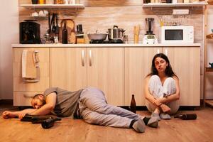 Alcoholic man lying on the floor near beaten wife surrounded by empty bottles. Drunk aggressive husband abusing injuring terrified helpless, afraid, beaten and panicked woman living in terror. photo