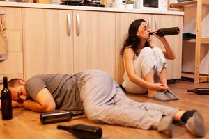 Drunk husband sleeping on kitchen floor after brutally beating his wife and being physically and psychologically affected. Aggressive man abusing injuring terrified, afraid, beaten and panicked woman . photo