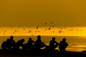 siluetas de personas pescar en un lago a puesta de sol. foto