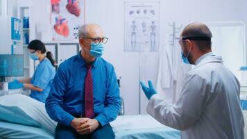 Senior man at doctor appointment during COVID-19 pandemic. Patient wearing mask and doctor in protective wear. Healthcare consultation, medicinal system. Private modern clinic photo