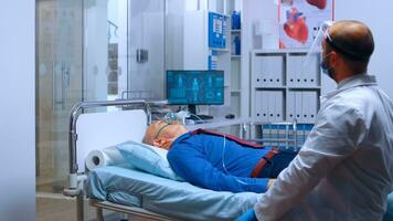 Doctor putting an oxygen mask to retired senior old man lying in hospital bed in modern private clinic. Help to breath during coronavirus covid-19 global health crisis outbreak photo