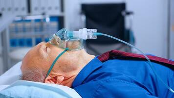 retrato de antiguo masculino paciente vistiendo oxígeno máscara acostado en hospital cama durante coronavirus covid-19 global salud pandemia. consiguiendo ayuda a aliento en contra respiratorio infección en moderno clínica foto