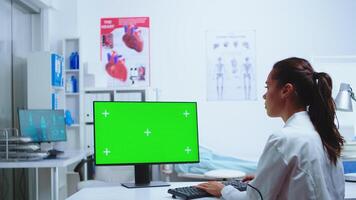 Medic writing diagnose on computer with green screen monitor while nurse is taking notes in the background. Computer with repleceable screen used by medicine specialist in hospital and wearing uniform. photo