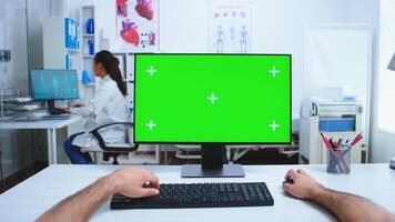 Pov of medical practitioner using computer with copy space available in hospital cabinet and doctor in the background. Medical physician in clinic cabinet working desktop with green screen available. photo