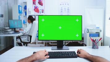 Pov of doctor hand working on computer with green screen in hospital cabinet. Medical physician in clinic cabinet working desktop with copy space available. photo