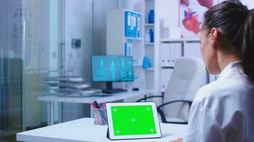 médico leyendo en tableta ordenador personal con verde pantalla en hospital gabinete acerca de un peligroso virus. asistente en azul médico uniforme. médico en salud clínica trabajando en tableta computadora con reemplazable pantalla haciendo medicina investigación. foto