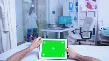 Pov shot of medic tapping on tablet pc with green screen in hospital cabinet. Doctor leaving from private clinic wearing white coat. Medic using tablet with chroma key on display in medical clinic. photo