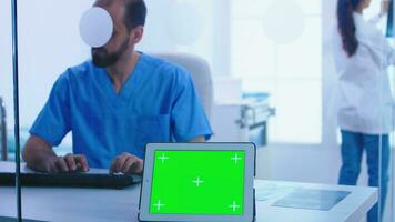 Assistant giving doctor patient x-ray and tablet pc with green screen display. View of tablet computer with chroma key through glass wall in hospital. photo