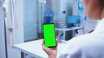 médico médico mirando a teléfono con verde pantalla en hospital gabinete y enfermero consiguiendo fuera de ascensor. cuidado de la salud especialista en hospital gabinete utilizando teléfono inteligente con Bosquejo. foto