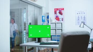 Computer with mock-up display in hospital cabinet and doctor entering in clinic. Desktop with blank and copy space green screen isolated available on display of medicine specialist in clinic cabinet. photo