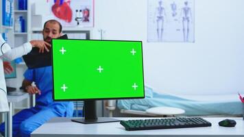 Computer display with copy space available in hospital cabinet and doctor holding x-ray. Desktop with replaceable green screen in medical clinic while doctor is checking patient radiography for diagnose. photo