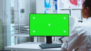 hembra médico trabajando en computadora con verde pantalla en privado clínica gabinete. asistente en uniforme. médico en blanco Saco trabajando en monitor con croma llave en clínica gabinete a cheque paciente diagnosticar. foto