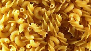 ongekookt fusilli en chifferi rigati pasta top visie, detailopname, laag sleutel. dik en ongezond voedsel. klassiek droog macaroni, roterend achtergrond. rauw verschillend macaroni pasta structuur draaien links video