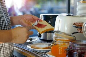 Asian woman uses a knife to spread blueberry jam on a slice of bread to eat for breakfast before going to work. Soft and selective focus. photo