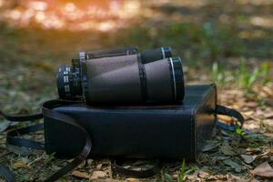 Binoculars and case lying on the ground in the forest It is a device for bird watching, animal viewing, and studying living things in the forest. Soft and selective focus. photo