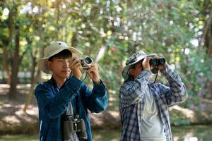 Two Asian boys use binoculars and a camera to study the local birds in a community forest. Soft and selective focus. photo