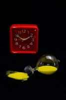 a red clock and an hourglass on black photo