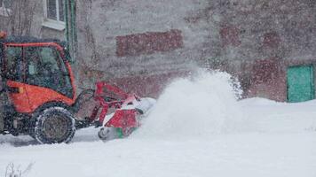 defocused röd traktor med snöplog rengöring snö trottoar på vinter- dagsljus häftig snöstorm video