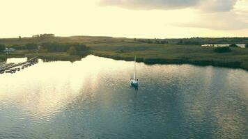 aéreo Visão em topo 1 iate dentro a mar às pôr do sol. a Sol e nuvens estão refletido dentro a água. uma iate este foi em uma viagem. video