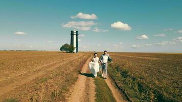 twee gelukkig jong mensen rennen samen Holding handen in een veld. vuurtoren in de veld. video