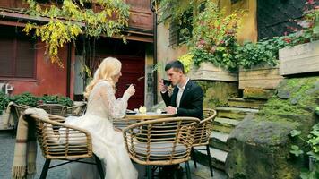 Boda día de el novia y novio en el cafetería. el novia y novio bebida té o café en un pequeño café con un abierto terraza. video