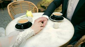 de tintje van de handen van de bruid en bruidegom. detailopname van de handen van de bruid en bruidegom en een kop van koffie. video