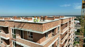 un jefe construcción ingeniero y un hembra arquitecto son inspeccionando un construcción sitio en el techo de un edificio. video