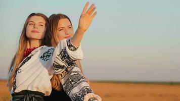 Two beautiful girls stand with their backs to each other in a wheat field at sunset. Two girls stretch out their hands to the sun at sunset. video