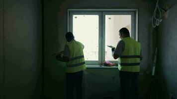 intern Konstruktion funktioniert. Silhouette von zwei Handwerker Verputzen das Wände in der Nähe von das Fenster. video